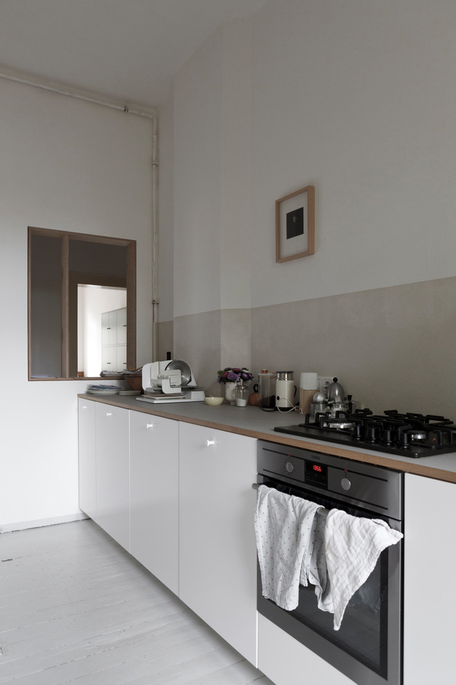 Small danish galley medium tone wood floor and gray floor enclosed kitchen photo in Leipzig with an undermount sink, flat-panel cabinets, white cabinets, gray backsplash, limestone backsplash, stainless steel appliances and no island