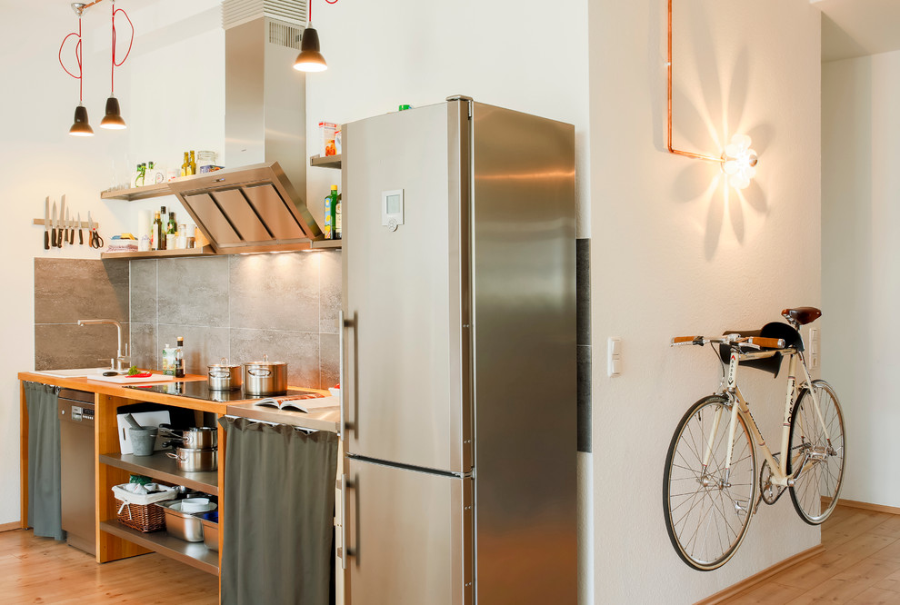 Inspiration for a small industrial single-wall open plan kitchen in Cologne with wood worktops, stainless steel appliances, no island, a built-in sink, medium wood cabinets, grey splashback and medium hardwood flooring.