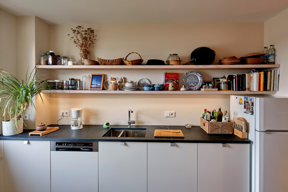Offene, Zweizeilige Moderne Küche mit flächenbündigen Schrankfronten, weißen Schränken, Küchenrückwand in Beige, dunklem Holzboden, Kücheninsel und schwarzer Arbeitsplatte in Essen