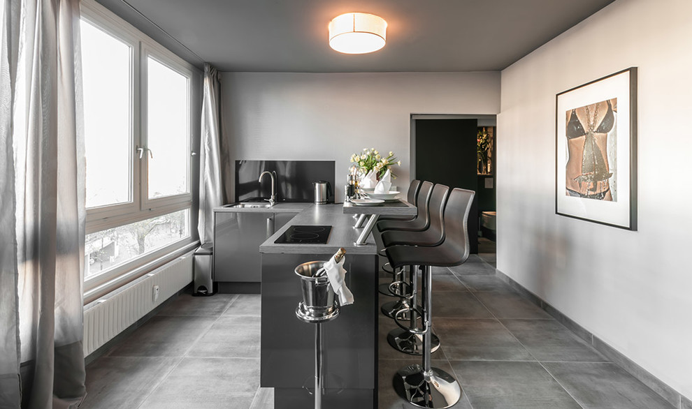 This is an example of a small contemporary kitchen in Berlin with an integrated sink, flat-panel cabinets, black cabinets, black splashback, concrete worktops, glass sheet splashback, stainless steel appliances and concrete flooring.