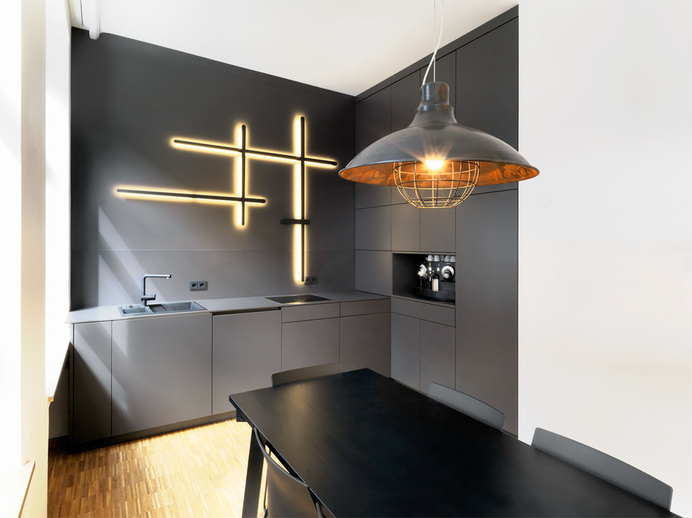 Diseño de cocina urbana pequeña con fregadero encastrado, armarios con paneles lisos, puertas de armario negras, salpicadero negro y suelo de madera en tonos medios