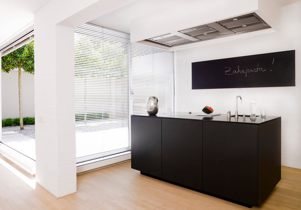 Cette photo montre une cuisine linéaire tendance de taille moyenne avec un évier encastré, un placard à porte plane, des portes de placard noires et parquet clair.