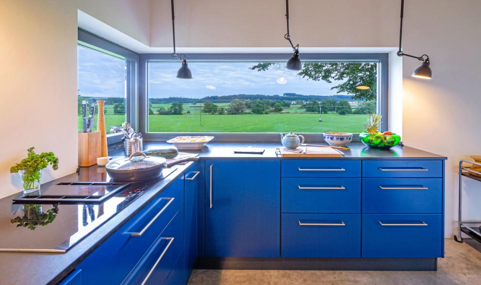 This is an example of a contemporary l-shaped open plan kitchen in Munich with blue cabinets and black worktops.