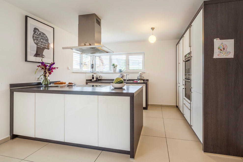 This is an example of a medium sized contemporary u-shaped enclosed kitchen in Other with flat-panel cabinets, white cabinets, wood worktops, a breakfast bar, beige floors, brown worktops and black appliances.