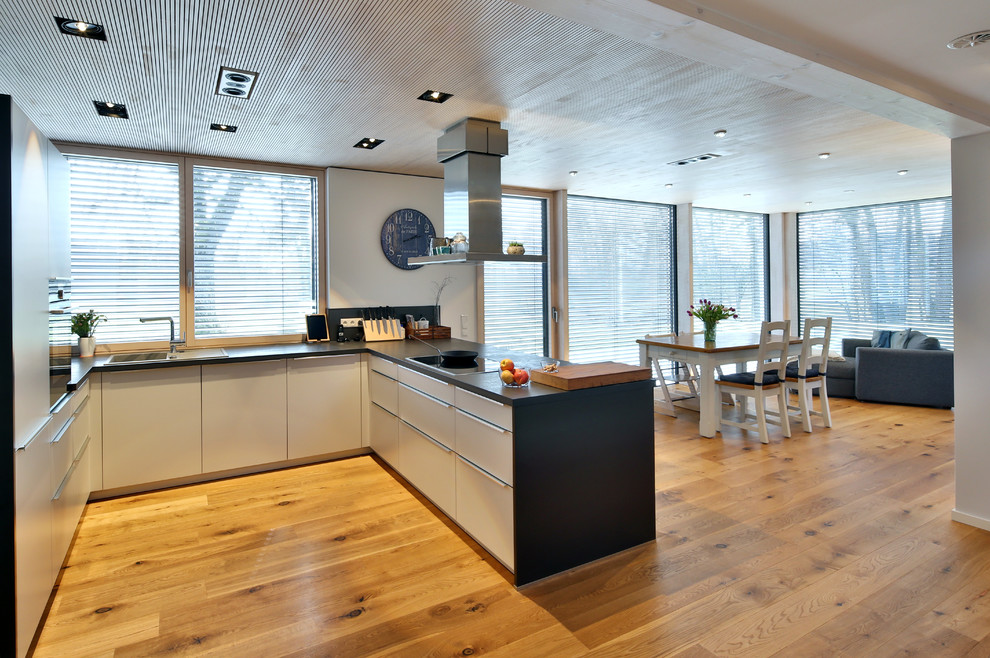 Immagine di una cucina design di medie dimensioni con penisola, lavello da incasso, ante lisce, ante bianche, pavimento in legno massello medio, pavimento marrone e top nero