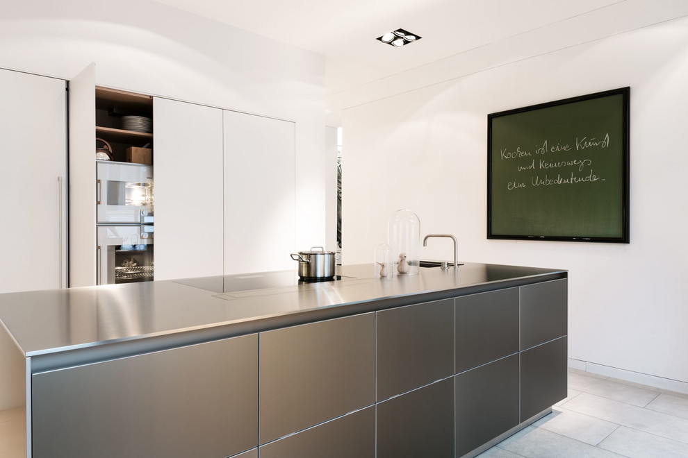 Foto på ett funkis linjärt kök, med en enkel diskho, släta luckor, skåp i rostfritt stål, bänkskiva i rostfritt stål, vita vitvaror, en köksö och kalkstensgolv