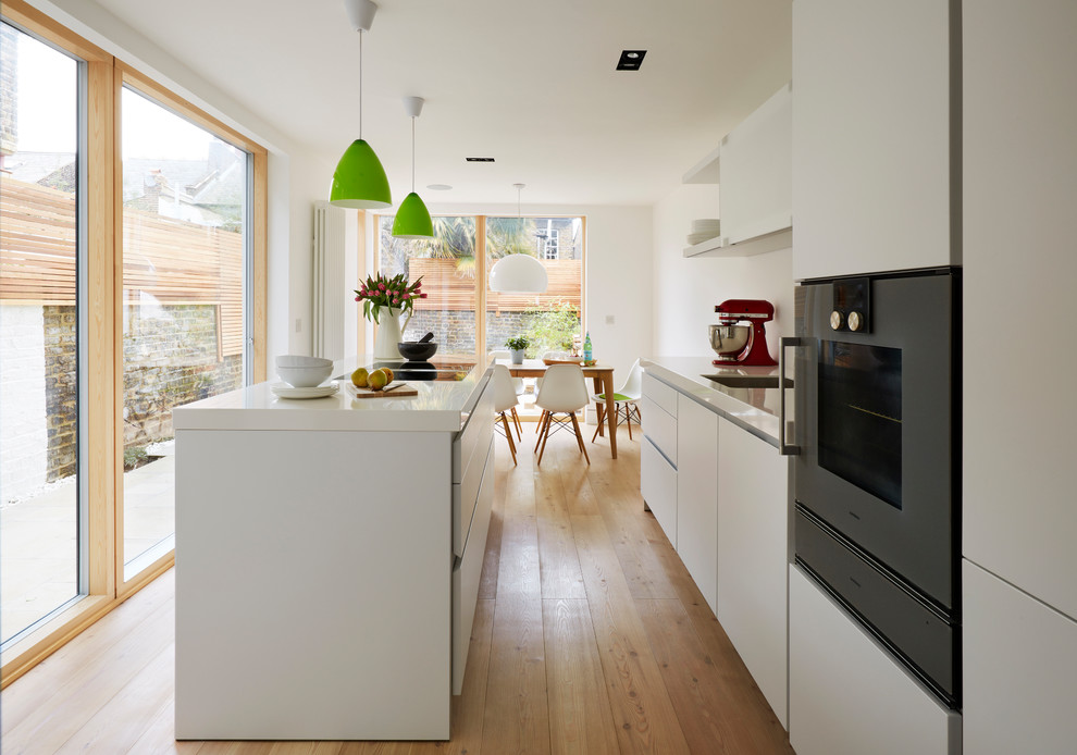 Foto på ett mellanstort funkis linjärt kök med öppen planlösning, med en nedsänkt diskho, vita skåp, vitt stänkskydd, mellanmörkt trägolv, en köksö, brunt golv och släta luckor