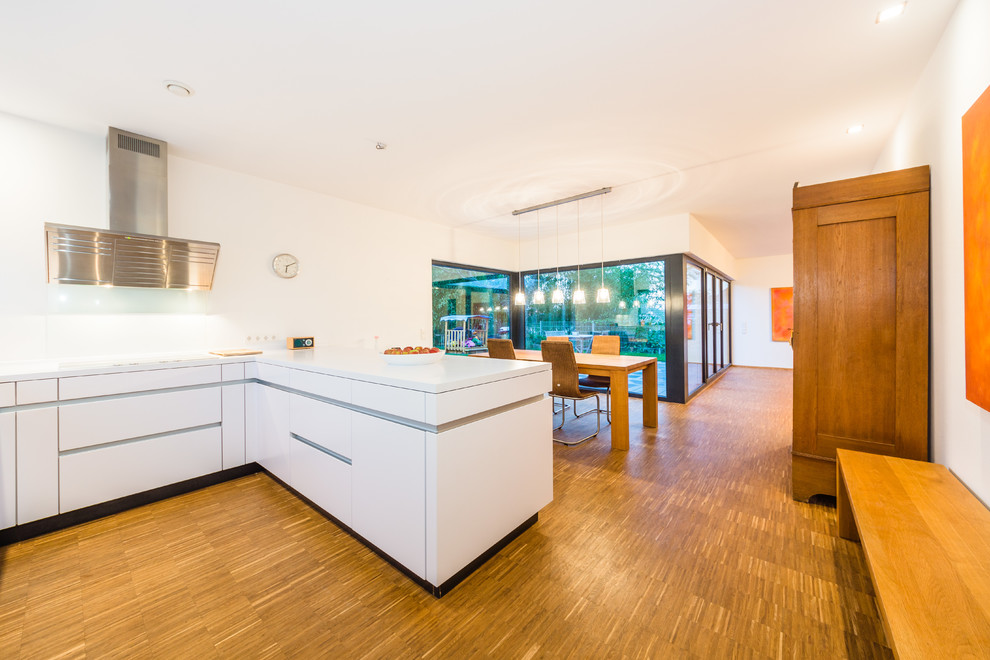 This is an example of a mid-sized contemporary l-shaped open plan kitchen in Frankfurt with flat-panel cabinets, white cabinets, white splashback, stone tile splashback, a peninsula, quartzite benchtops and medium hardwood floors.