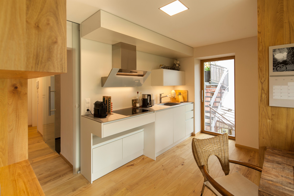 Einzeilige Moderne Wohnküche ohne Insel mit weißen Schränken, Edelstahl-Arbeitsplatte und braunem Holzboden in Sonstige