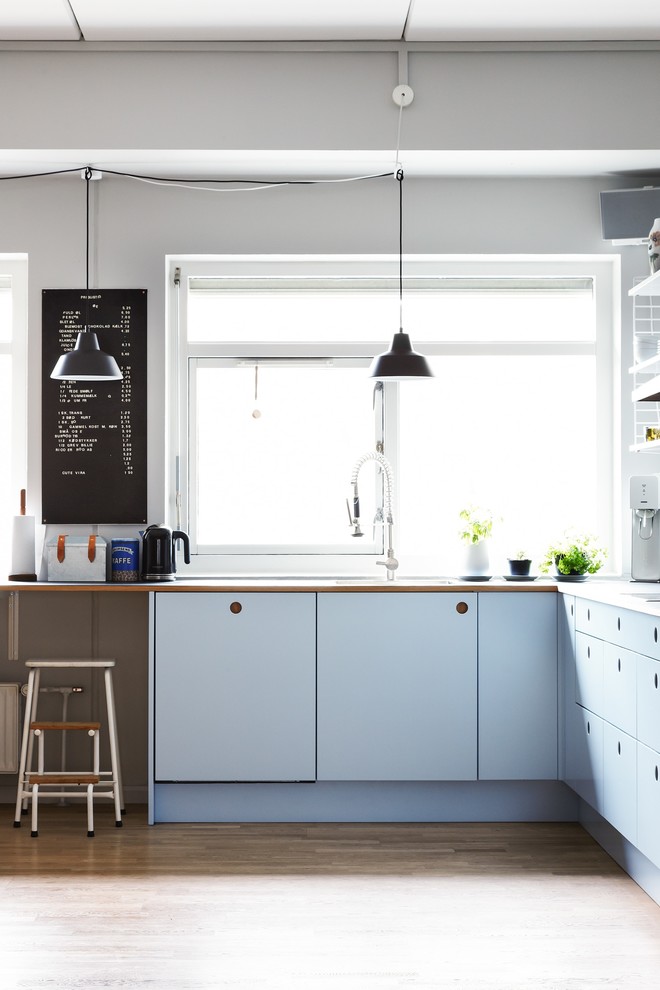 Modelo de cocinas en L escandinava abierta con puertas de armario azules y suelo de madera clara