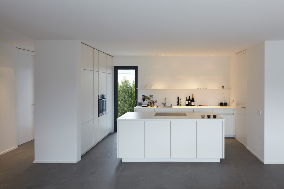 Diseño de cocina minimalista grande abierta con armarios con paneles lisos, puertas de armario blancas, salpicadero blanco, electrodomésticos de acero inoxidable, suelo de pizarra, una isla y fregadero encastrado
