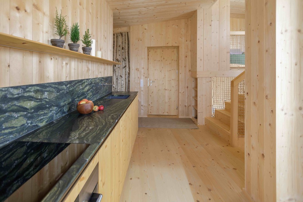 Inredning av ett nordiskt mellanstort linjärt kök med öppen planlösning, med en integrerad diskho, släta luckor, skåp i mellenmörkt trä, bänkskiva i onyx, flerfärgad stänkskydd, rostfria vitvaror, ljust trägolv och brunt golv