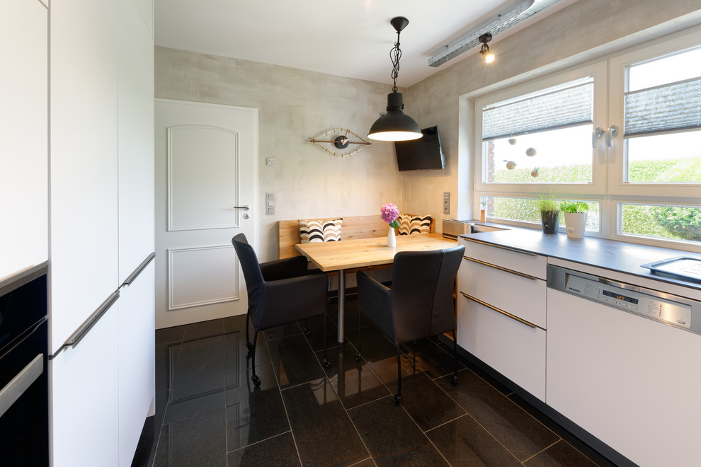 エッセンにある中くらいなインダストリアルスタイルのおしゃれなキッチン (フラットパネル扉のキャビネット、白いキャビネット、白い調理設備、黒い床) の写真