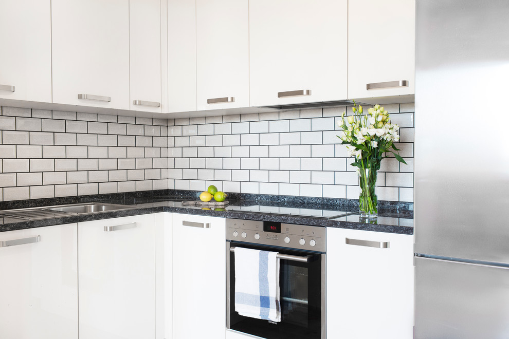 Inspiration for a small contemporary l-shaped kitchen in Berlin with white cabinets, granite worktops, white splashback, metro tiled splashback, stainless steel appliances and light hardwood flooring.