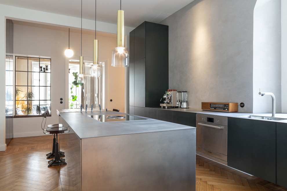 Design ideas for a contemporary galley kitchen in Berlin with a submerged sink, flat-panel cabinets, black cabinets, stainless steel appliances, medium hardwood flooring, an island, brown floors and grey worktops.