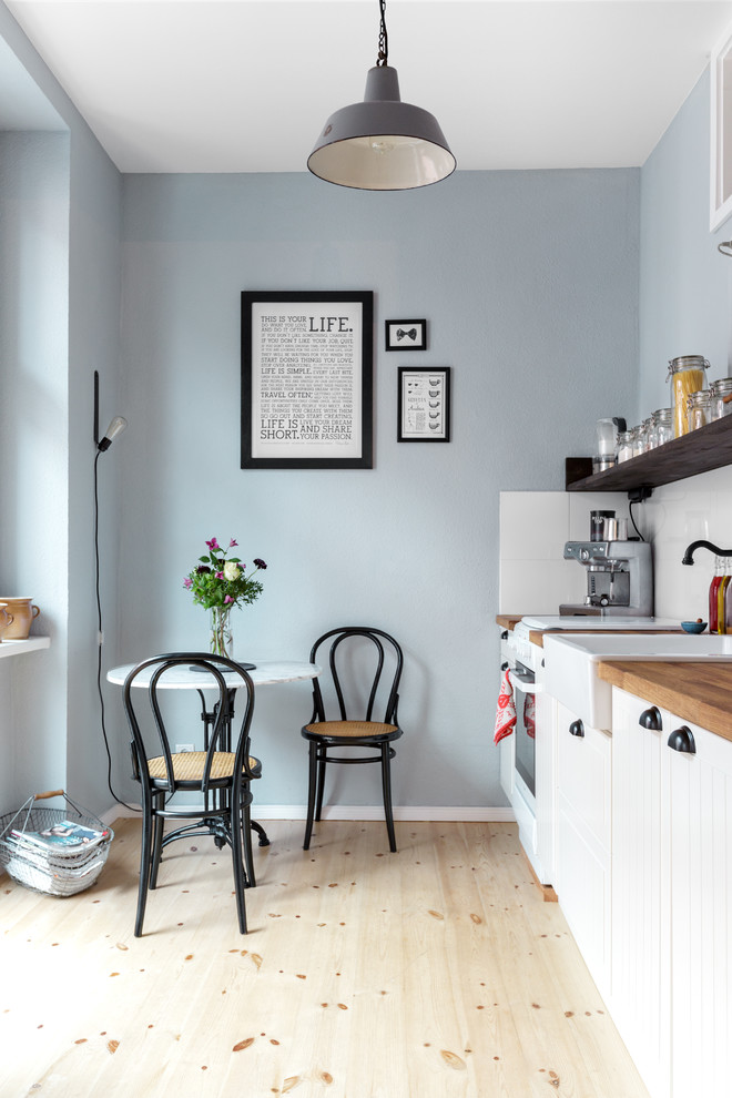 Example of a small danish single-wall light wood floor eat-in kitchen design in Berlin with a farmhouse sink, white cabinets, wood countertops, white backsplash, recessed-panel cabinets, white appliances, ceramic backsplash and no island