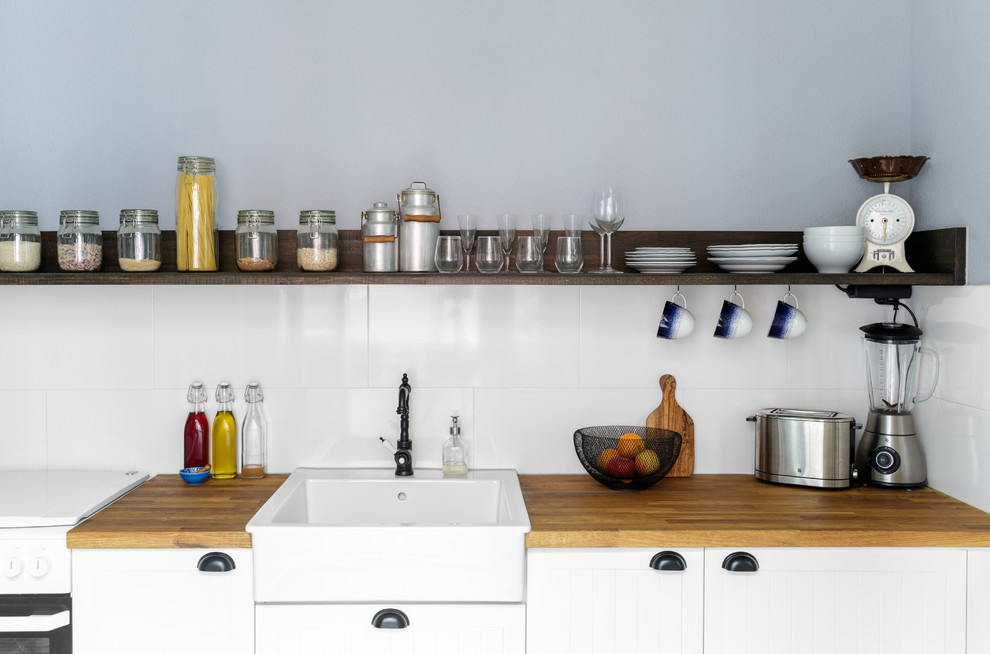 This is an example of a medium sized country single-wall enclosed kitchen in Berlin with a single-bowl sink, white cabinets, wood worktops, white splashback, ceramic splashback, stainless steel appliances and no island.