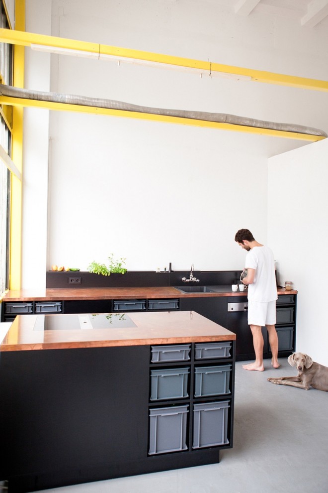 Esempio di una cucina industriale di medie dimensioni con lavello da incasso, ante nere, top in rame, paraspruzzi bianco, elettrodomestici neri e pavimento in cemento