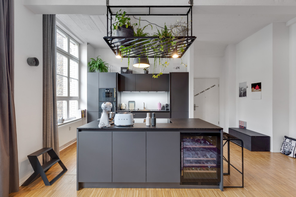 Zweizeilige Stilmix Küche mit flächenbündigen Schrankfronten, grauen Schränken, schwarzen Elektrogeräten, braunem Holzboden, Kücheninsel, braunem Boden und schwarzer Arbeitsplatte in Frankfurt am Main
