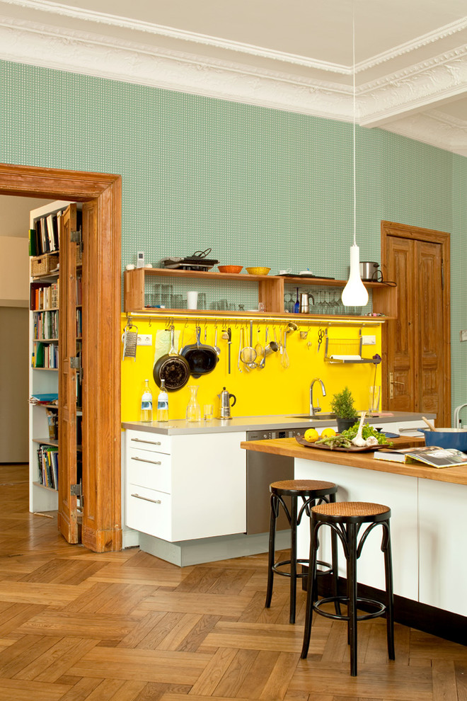 Foto på ett stort eklektiskt kök med öppen planlösning, med släta luckor, vita skåp, gult stänkskydd, rostfria vitvaror, mellanmörkt trägolv, en köksö, en integrerad diskho och bänkskiva i rostfritt stål