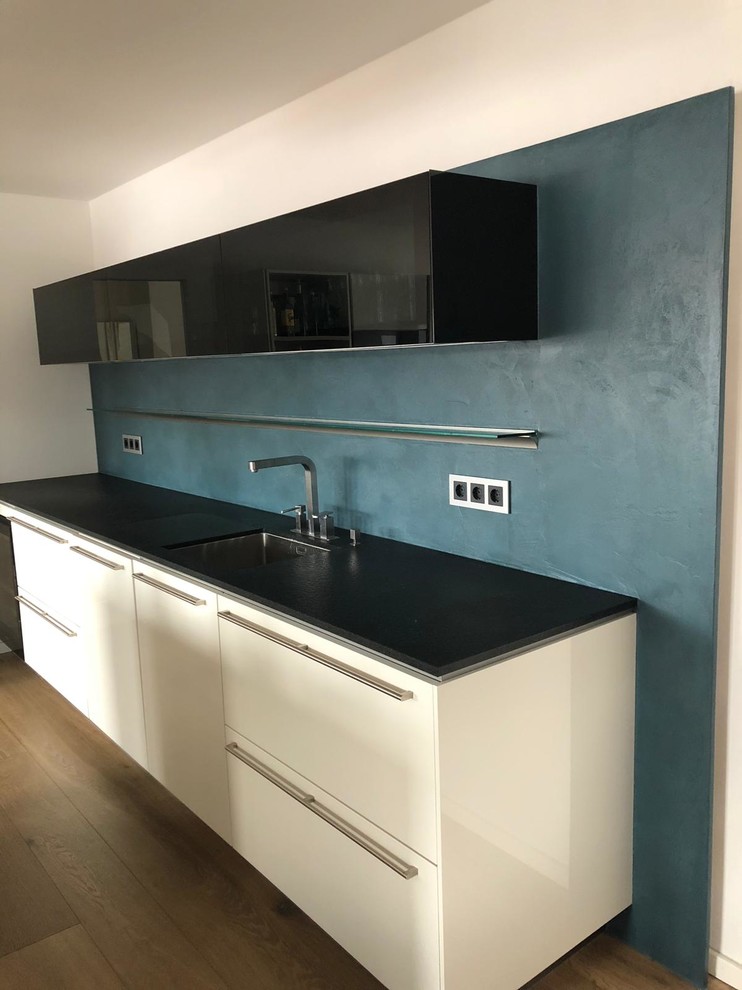 Moderne Küche mit Granit-Arbeitsplatte, Küchenrückwand in Blau, dunklem Holzboden und schwarzer Arbeitsplatte in München