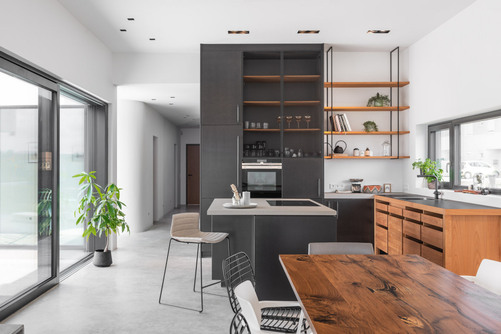 This is an example of an expansive contemporary l-shaped kitchen/diner in Other with concrete worktops, concrete flooring, an island, a submerged sink, flat-panel cabinets, black cabinets, window splashback, black appliances, grey floors and grey worktops.