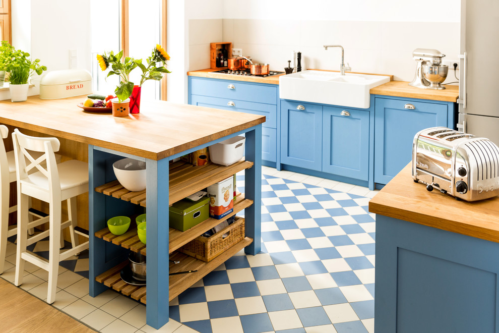 ケルンにあるお手頃価格の小さな北欧スタイルのおしゃれなキッチン (ダブルシンク、シェーカースタイル扉のキャビネット、青いキャビネット、木材カウンター、白いキッチンパネル、セラミックタイルのキッチンパネル、シルバーの調理設備、セラミックタイルの床) の写真