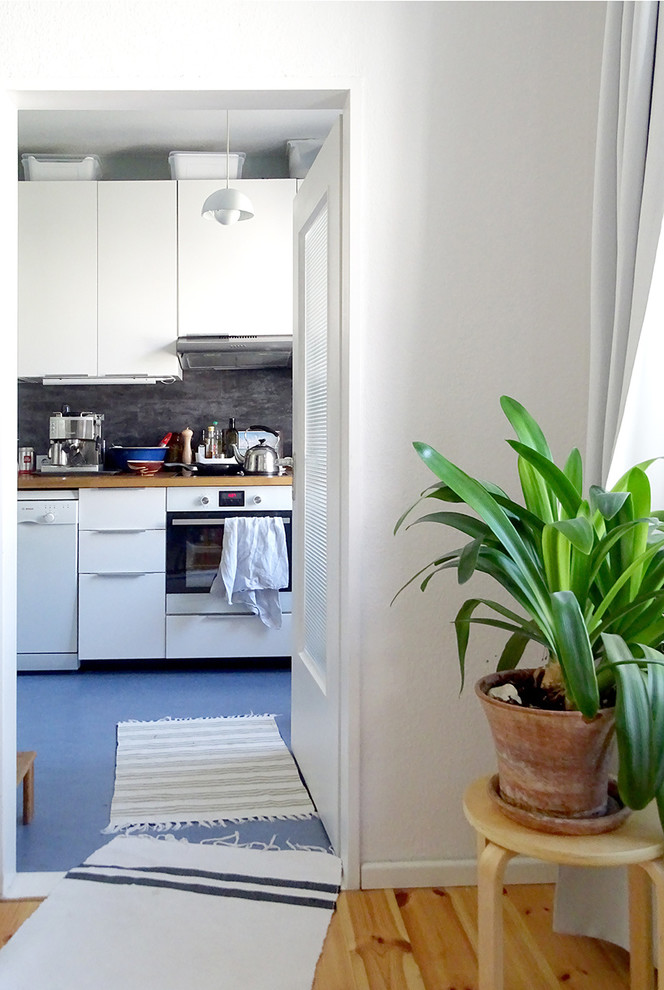 Inredning av ett skandinaviskt avskilt, mellanstort linjärt kök, med en enkel diskho, släta luckor, vita skåp, träbänkskiva, grått stänkskydd, rostfria vitvaror, linoleumgolv, stänkskydd i skiffer och blått golv