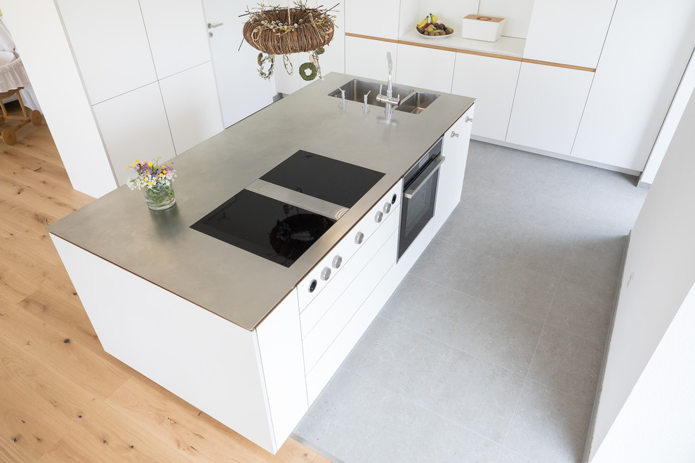 Inredning av ett modernt stort grå linjärt grått kök med öppen planlösning, med en dubbel diskho, släta luckor, vita skåp, bänkskiva i rostfritt stål, vitt stänkskydd, rostfria vitvaror, cementgolv, en köksö och grått golv