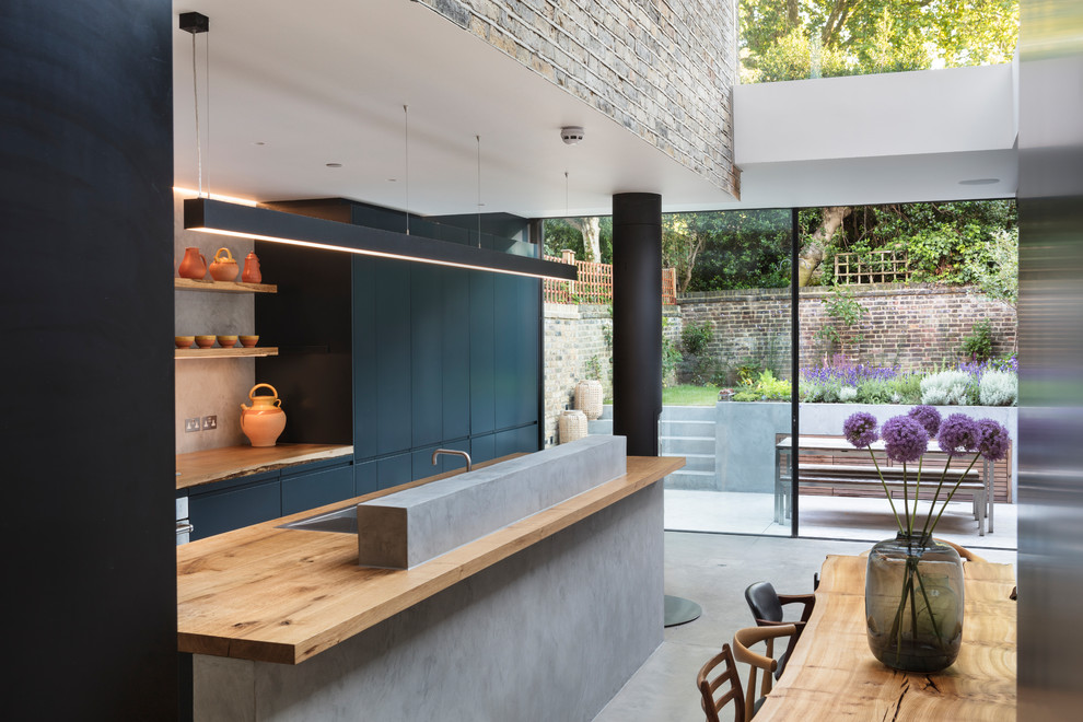Photo of a large contemporary galley open plan kitchen in London with flat-panel cabinets, blue cabinets, wood worktops, grey splashback and an island.