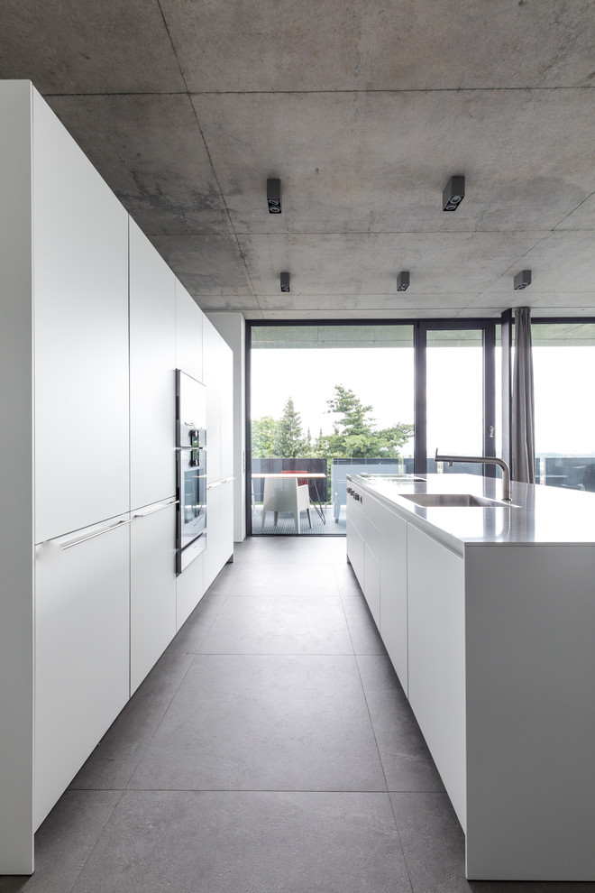 Example of a large minimalist galley gray floor open concept kitchen design in Frankfurt with a single-bowl sink, white cabinets, stainless steel appliances, an island, flat-panel cabinets and white countertops