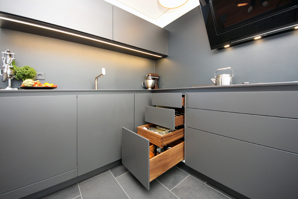 Moderne Küche in L-Form mit Einbauwaschbecken, flächenbündigen Schrankfronten, grauen Schränken, Küchenrückwand in Grau und schwarzen Elektrogeräten in Sonstige