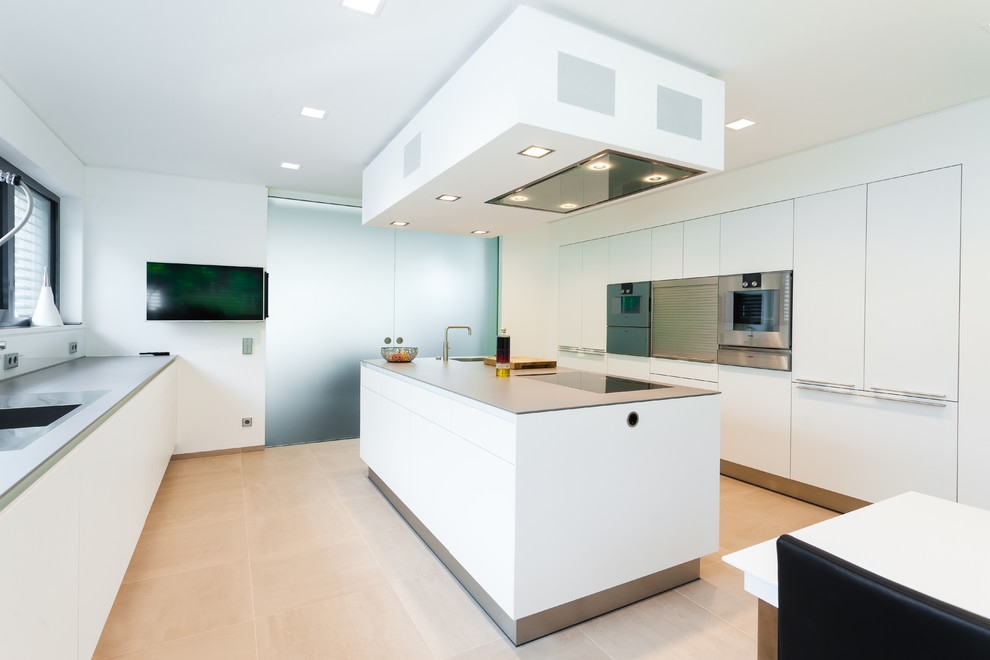 Modelo de cocina lineal contemporánea abierta con puertas de armario blancas, salpicadero blanco, electrodomésticos de acero inoxidable y una isla