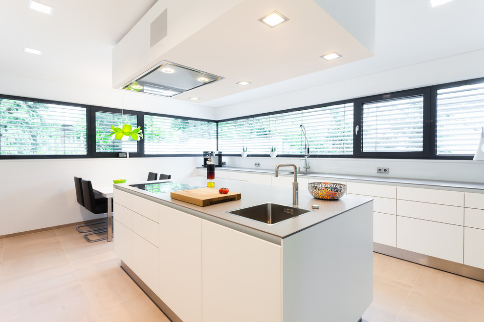 Imagen de cocina lineal actual abierta con puertas de armario blancas, salpicadero blanco y una isla