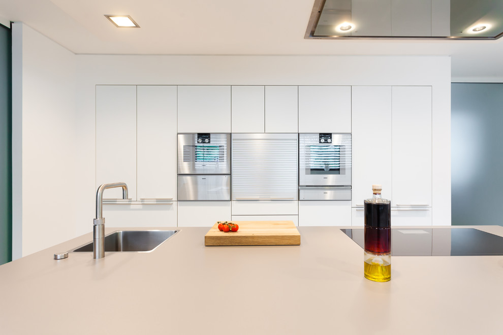 Идея дизайна: прямая кухня-гостиная в современном стиле с белыми фасадами, белым фартуком, техникой из нержавеющей стали и островом