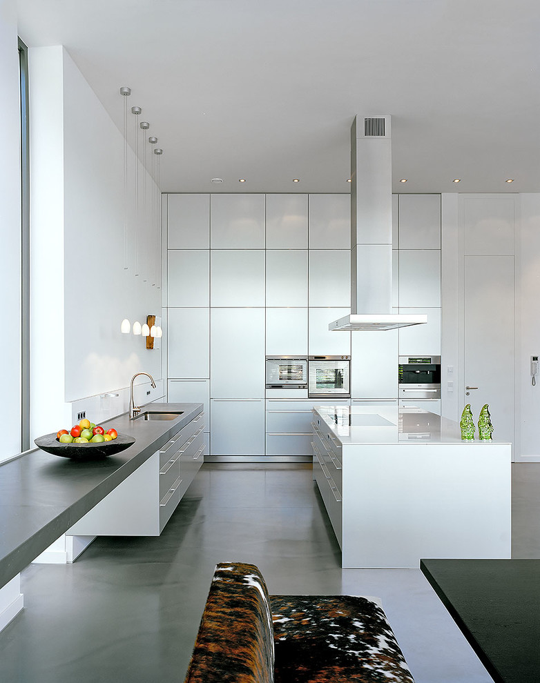 Große Moderne Wohnküche in L-Form mit Einbauwaschbecken, flächenbündigen Schrankfronten, weißen Schränken, Glas-Arbeitsplatte, Küchengeräten aus Edelstahl, Vinylboden, zwei Kücheninseln und grauem Boden in Köln