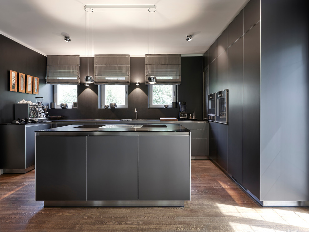 Medium sized contemporary u-shaped enclosed kitchen in Munich with flat-panel cabinets, black cabinets, black splashback, black appliances, medium hardwood flooring, an island, brown floors and black worktops.