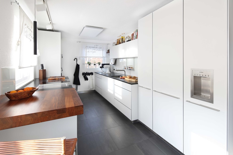 Enclosed kitchen - large contemporary galley black floor and ceramic tile enclosed kitchen idea in Stuttgart with an undermount sink, flat-panel cabinets, white cabinets, granite countertops, white backsplash, glass sheet backsplash, black countertops, paneled appliances and no island