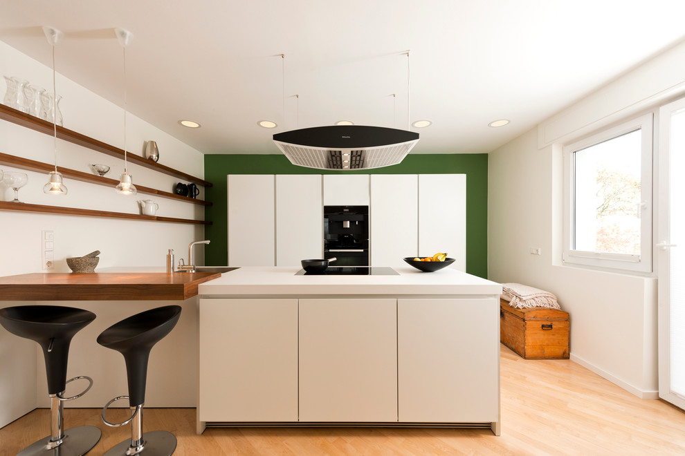 Modelo de cocina actual grande cerrada con fregadero de un seno, armarios con paneles lisos, puertas de armario blancas, electrodomésticos negros, suelo de madera en tonos medios y península