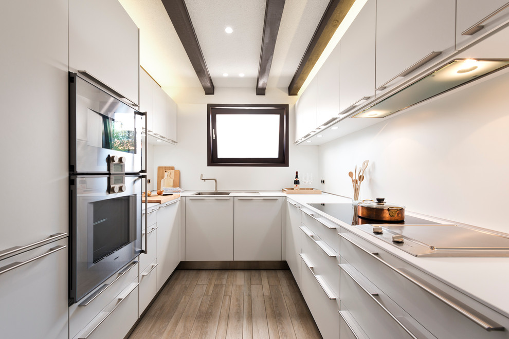 Medium sized contemporary u-shaped enclosed kitchen in Berlin with a built-in sink, flat-panel cabinets, white cabinets, white splashback, stainless steel appliances, medium hardwood flooring and no island.