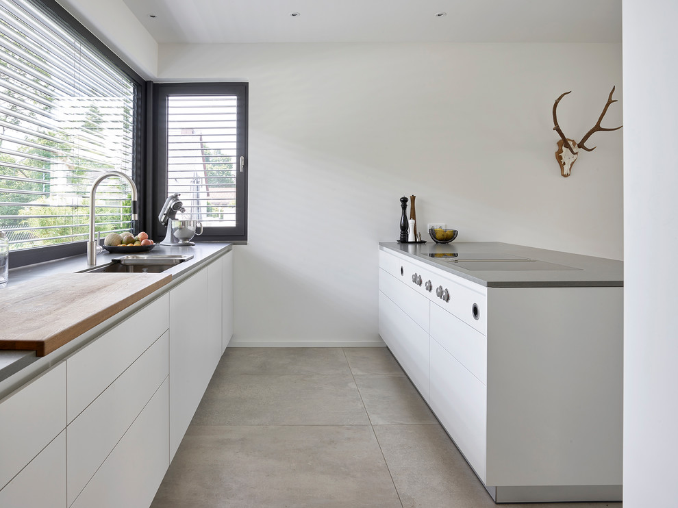 Exemple d'une cuisine parallèle tendance de taille moyenne avec un évier intégré, un placard à porte plane, des portes de placard blanches, un plan de travail en inox, îlot, un sol gris et un plan de travail gris.
