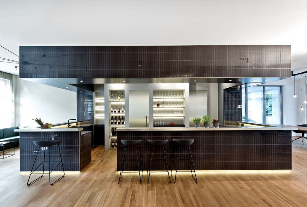 Immagine di una grande cucina ad ambiente unico minimal con pavimento in legno massello medio, nessun'anta, paraspruzzi grigio e penisola
