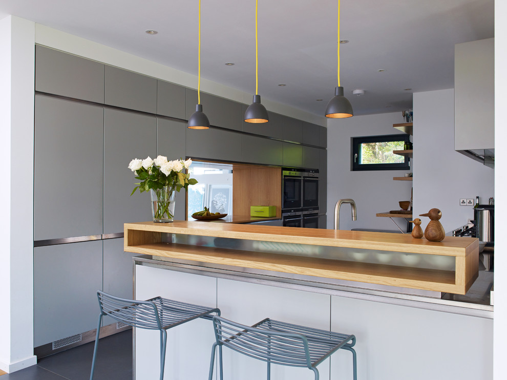 На фото: кухня-гостиная среднего размера в современном стиле с плоскими фасадами, серыми фасадами, техникой под мебельный фасад, полуостровом и серым полом