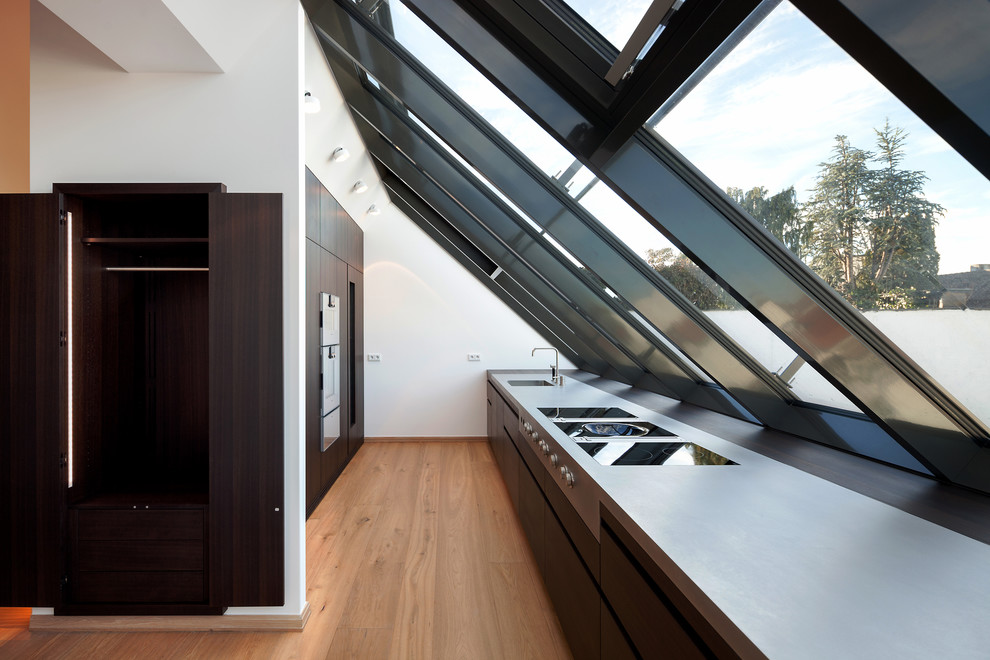 Mid-sized minimalist galley medium tone wood floor enclosed kitchen photo in Munich with an integrated sink, flat-panel cabinets, dark wood cabinets, paneled appliances and no island