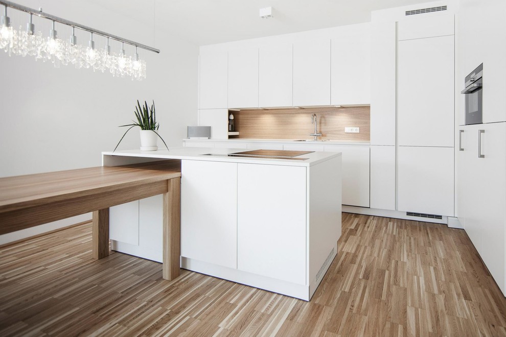 Example of a minimalist single-wall medium tone wood floor open concept kitchen design in Other with a drop-in sink, flat-panel cabinets, white cabinets, brown backsplash, black appliances and an island
