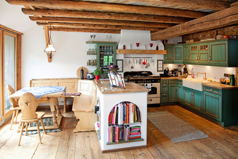 Foto på ett lantligt kök, med en rustik diskho, gröna skåp, träbänkskiva, vitt stänkskydd, vita vitvaror, mellanmörkt trägolv, en halv köksö och luckor med infälld panel