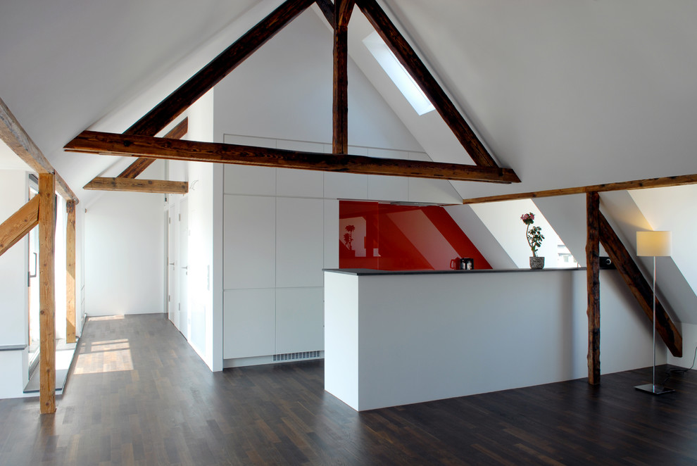 Стильный дизайн: кухня-гостиная среднего размера в современном стиле с плоскими фасадами, белыми фасадами, красным фартуком, темным паркетным полом, полуостровом и коричневым полом - последний тренд