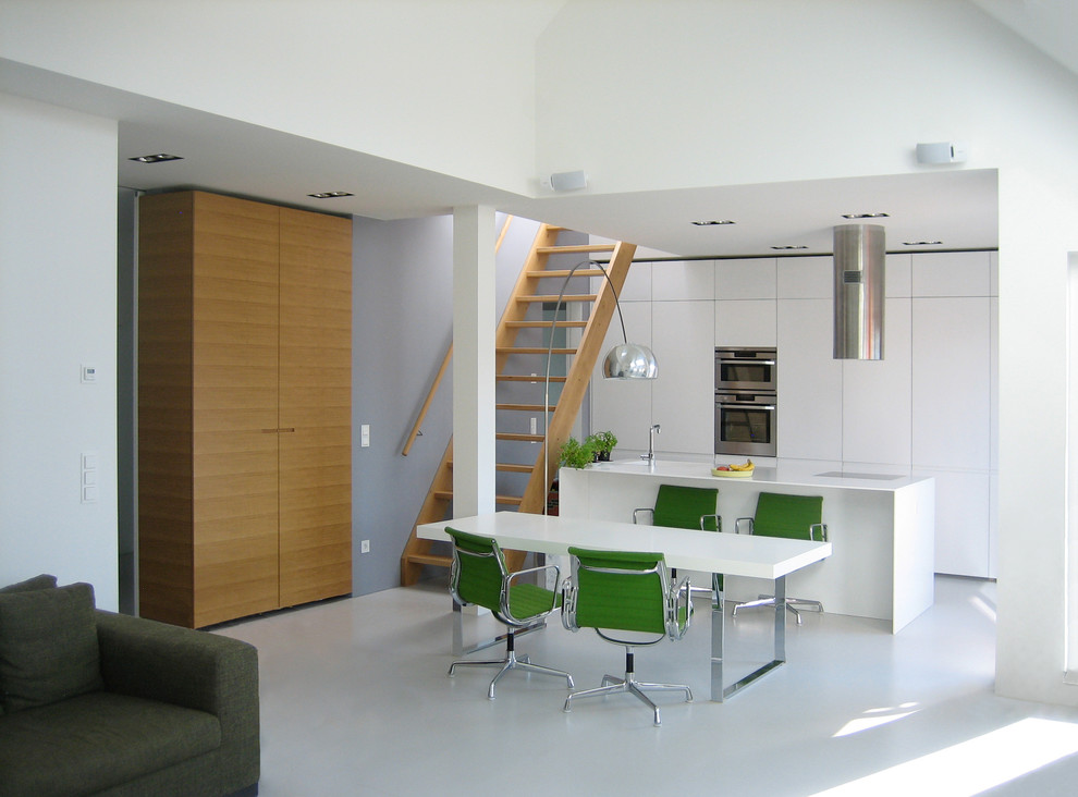 Modelo de cocina actual de tamaño medio abierta con armarios con paneles lisos, una isla, puertas de armario blancas y electrodomésticos de acero inoxidable