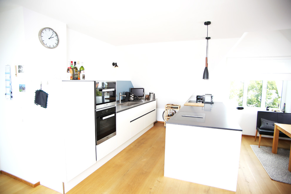 Foto de cocina comedor minimalista de tamaño medio con fregadero de un seno, armarios con paneles lisos, puertas de armario blancas, encimera de acero inoxidable, electrodomésticos de acero inoxidable y una isla