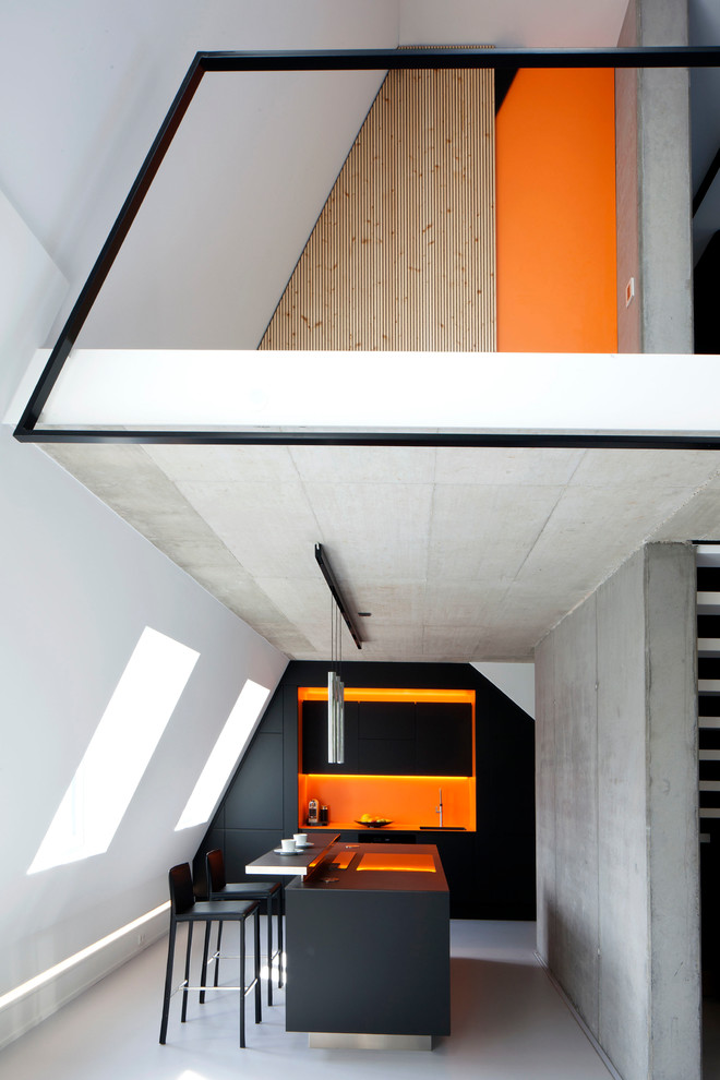 Modelo de cocina minimalista abierta con armarios con paneles lisos, puertas de armario negras, salpicadero naranja, una isla, suelo gris y encimeras negras